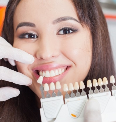 Young woman smiling as dentist holds veneers near her teeth