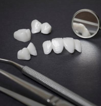 Several white dental crowns and veneers on table next to dental mirror