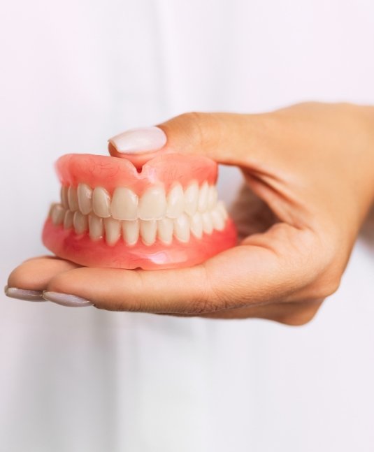 Hand holding a set of full dentures in San Jose