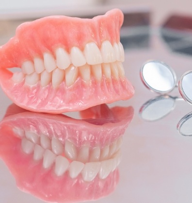 Dentures resting on table next to two dental mirrors