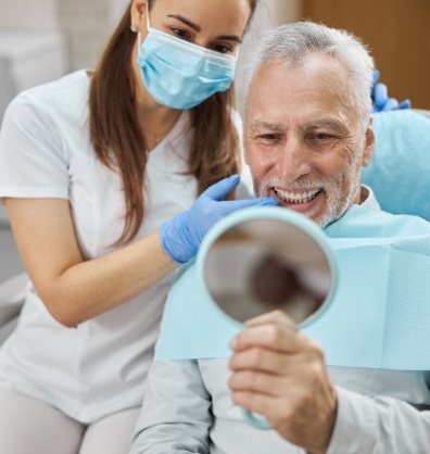 Senior dental patient looking in mirror at his new smile