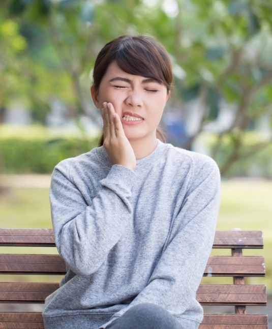 Woman wincing and holding her cheek in pain needing emergency dentist in San Jose