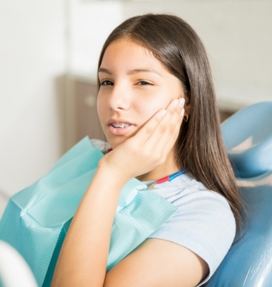 Young woman in dental chair holding her cheek in pain