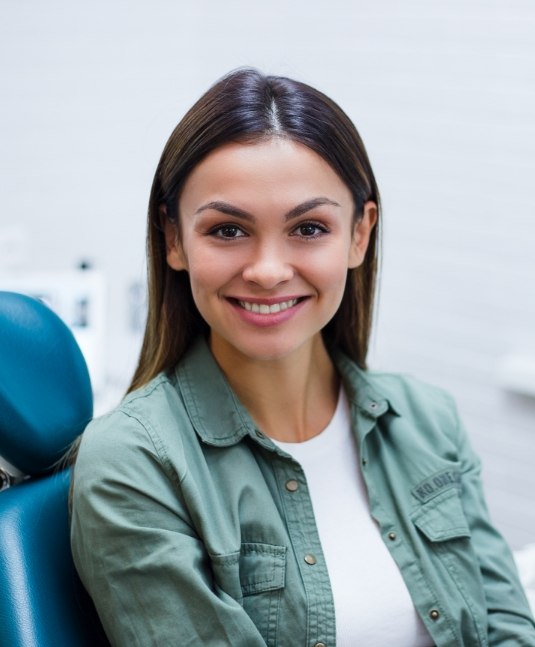 Young woman in green jacket smiling and sitting in dental chair