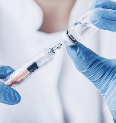 Person drawing syringe from vial of clear liquid