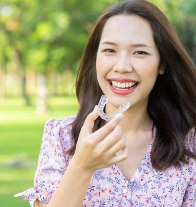 Smiling woman holding an Invisalign clear aligner