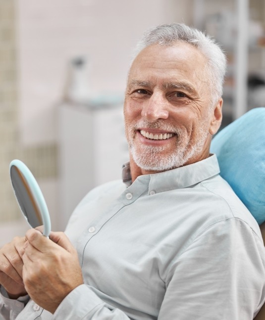 Senior man smiling in dental chair and holding a mirror