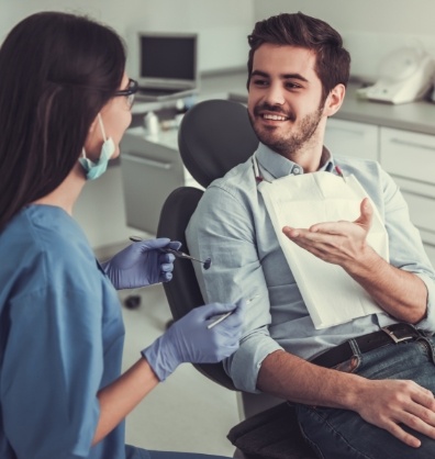 Young man in dental chair talking to dental team member