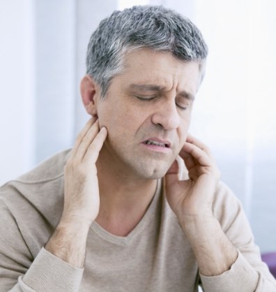 Man wincing and holding the sides of his jaw in pain