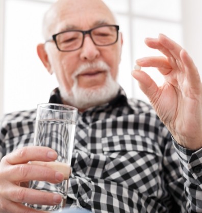 Senior man holding a pill and a glass of water