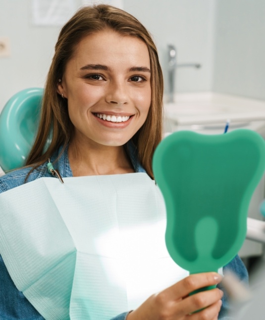 Young woman in dental chair smiling and holding a mirror