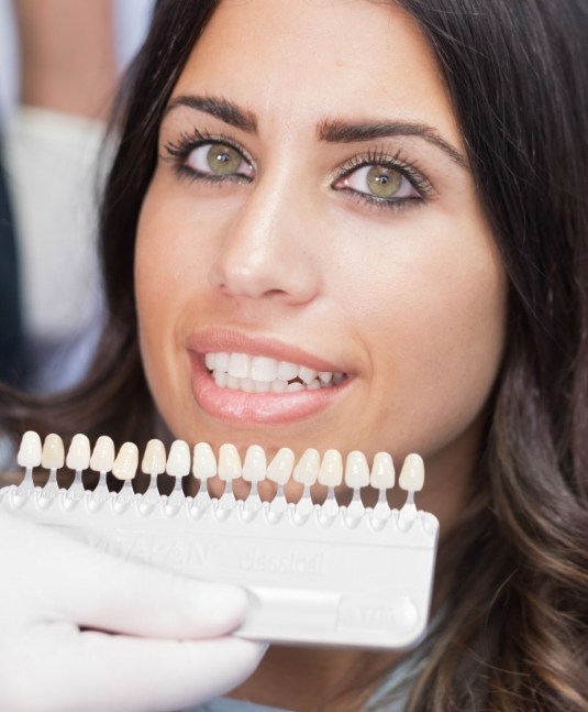 Woman smiling while dentist holds row of veneers in San Jose